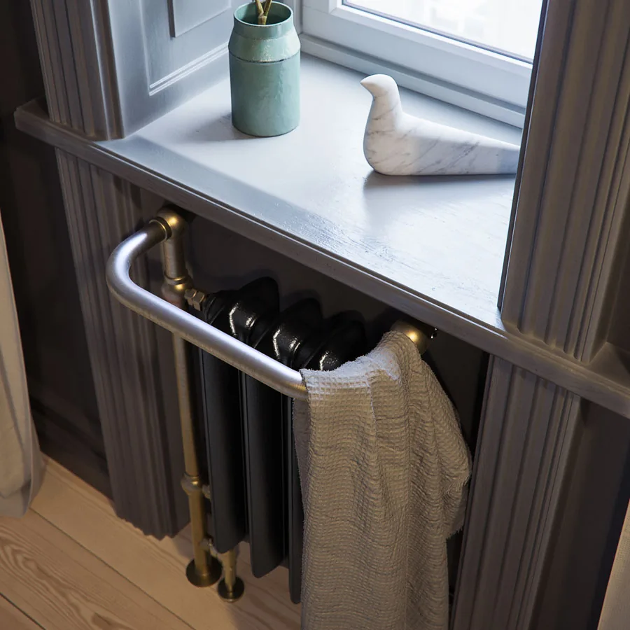 Gietijzeren handdoekradiator Plain Towel Rail in zwart onder een vensterbank, met handdoek over het frame