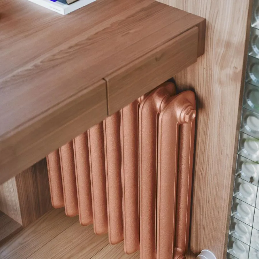 Gietijzeren radiator Plain in een koperkleurige afwerking onder een houten blad
